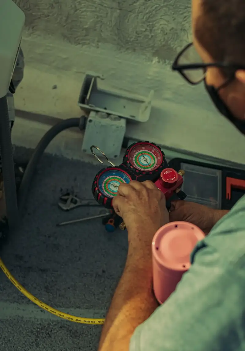 A technician reading a manifold gauge set beside an outdoor unit